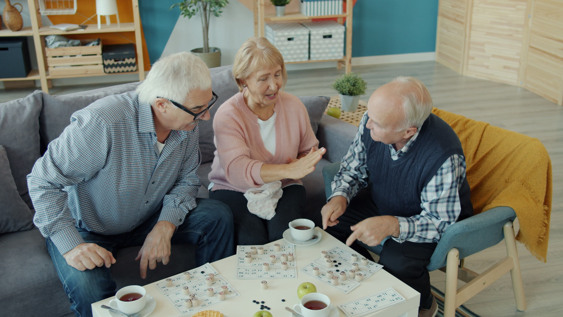 Drei ältere Menschen spielen zusammen ein Gesellschaftsspiel am Wohnzimmertisch