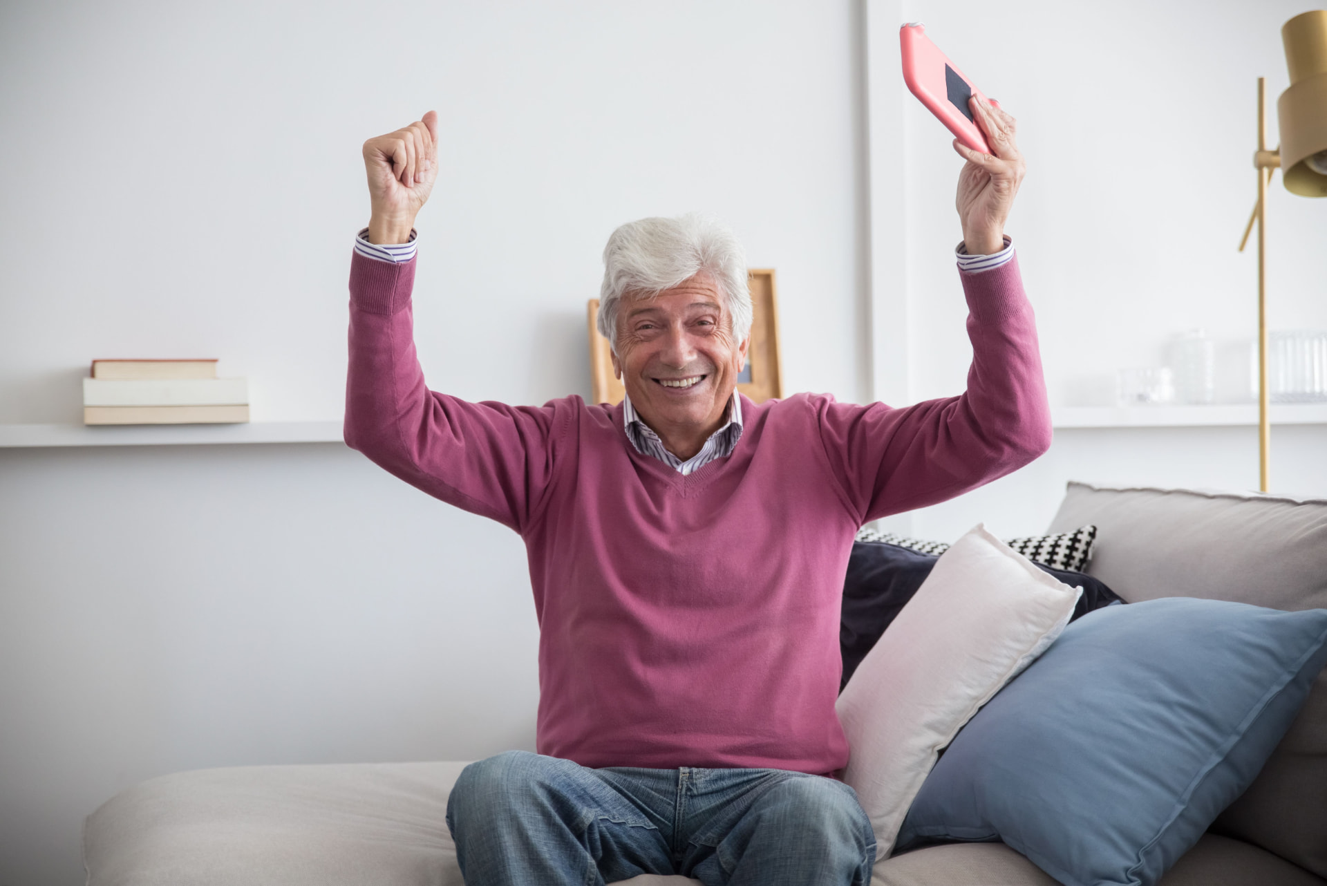 Älterer Mann freut sich mit erhobenen Armen auf seinem Sofa